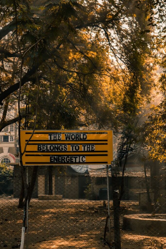 The Art of Drawing Readers In: Your attractive post title goes here Yellow sign with motivational text in a sunlit park setting, capturing a warm, inspiring vibe.