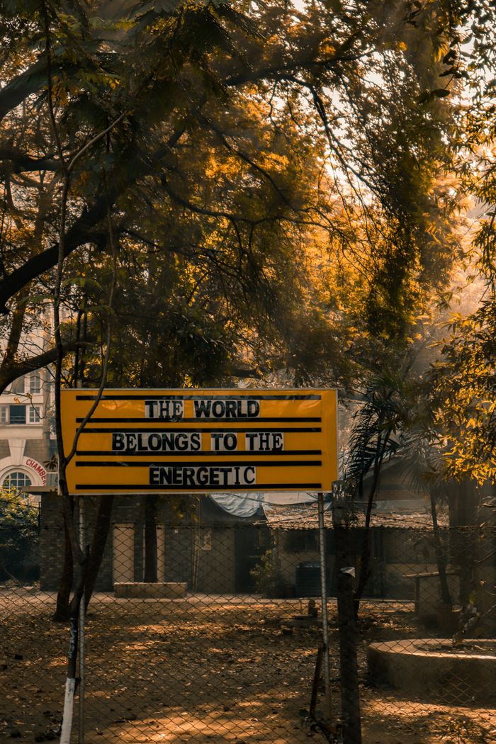 The Art of Drawing Readers In: Your attractive post title goes here Yellow sign with motivational text in a sunlit park setting, capturing a warm, inspiring vibe.